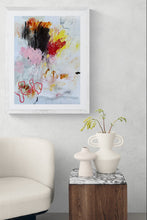 the painting on a wall above a white armchair with a small table and decorative items